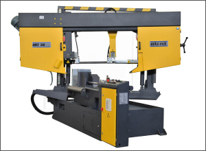 A large gray industrial saw with yellow panels is shown against a white background. A long horizontal beam spans two yellow covers above the work area. The heavy base supports the machine below. A dark hose curves from the left side.